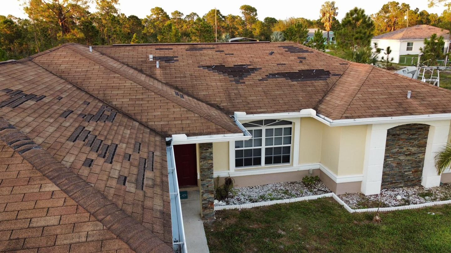 Aerial drone view of a house roof with wind and hail damaged shingles missing in patches